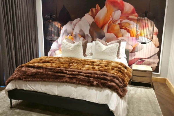 The wallpaper features a vibrant, oversized floral mural. It includes vivid colors such as lush greens, bold reds, deep purples, and bright yellows. The large flowers contrasted against the leaves create a dynamic and lively appearance. This eye-catching design adds an elegant and luxurious touch to any bedroom setting.