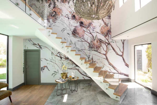A nature-themed mural wallpaper features elements like lush green leaves, floral motifs, and delicate branches. Earthy tones of greens, browns, and touches of soft blues dominate the design. The artwork brings in a lively yet serene ambiance with organic shapes inspired by nature's elegance. Ideal for making a space feel fresh and vibrant.
