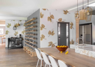 A standout element in this modern kitchen and dining area is the leaf-patterned wallpaper. It features elegant botanical motifs in shades of green, beige, and soft gold, creating a serene backdrop that complements the space. The intricate leaf designs add texture and depth to the walls, enhancing the natural aesthetic. This wallpaper seamlessly ties together the room's contemporary elements with a touch of nature-inspired elegance.