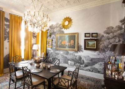 Scenic mural wallpaper featuring lush landscapes with earthy browns, greens, and sky blues. Vibrant florals in reds and yellows interspersed among intricate patterns. Detailed tree branches with dappled leaves create a rich, nature-inspired tapestry.