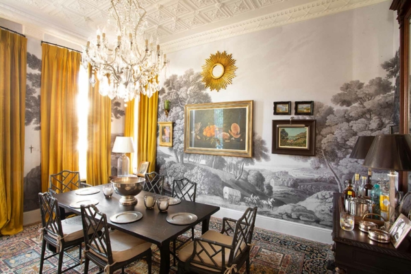 Scenic mural wallpaper featuring lush landscapes with earthy browns, greens, and sky blues. Vibrant florals in reds and yellows interspersed among intricate patterns. Detailed tree branches with dappled leaves create a rich, nature-inspired tapestry.