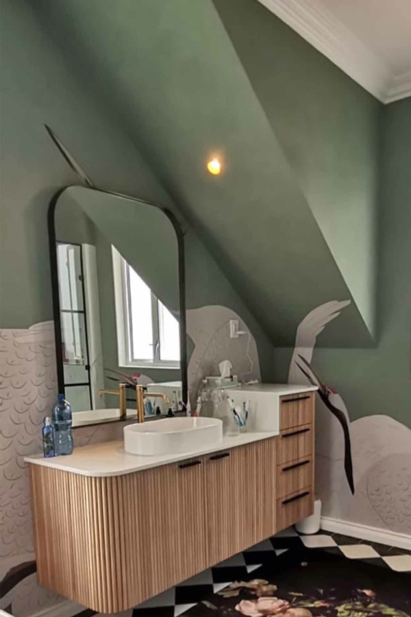 The wallpaper features a stunning crane mural with detailed illustrations of cranes in flight. The primary colors include graceful shades of white, grey, and black for the cranes' bodies and wings, all set against a serene background that complements their elegance. Hints of nature-inspired hues such as light blues and soft greens add depth to the scene, making it an eye-catching centerpiece in the bathroom’s design.