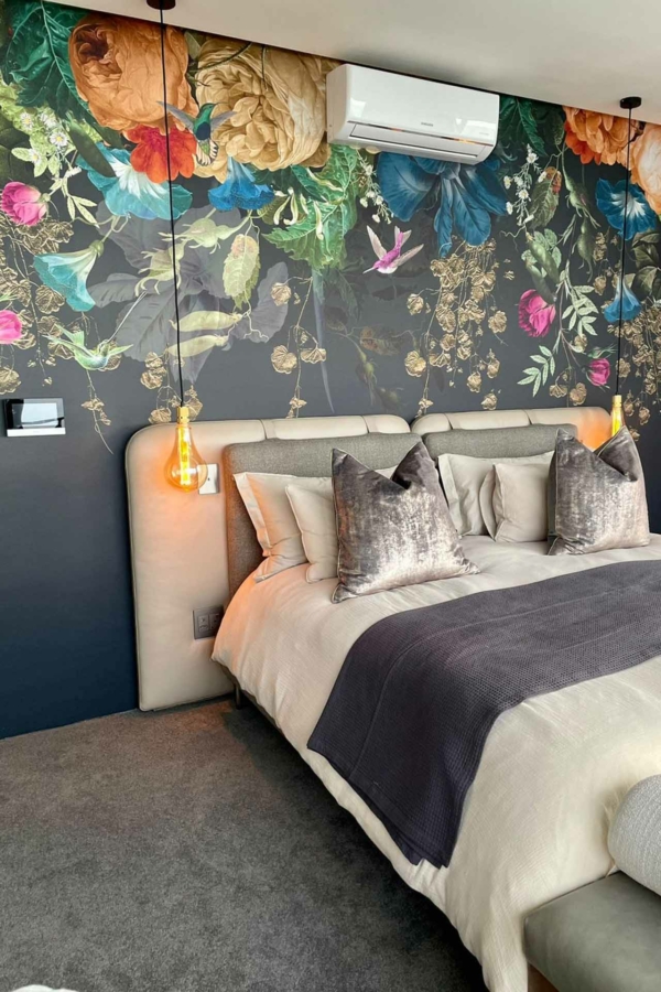 The wallpaper features a vibrant floral mural in dark tones, with rich hues of deep burgundy, midnight blue, forest green, and accents of gold. The intricate design includes various flowers and foliage, creating a dynamic and elegant backdrop for the bedroom.