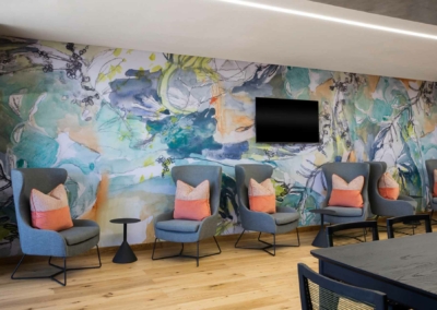 Colorful abstract mural featuring vivid shades of blue, red, yellow, green, and purple. Swirling patterns, geometric shapes, and bold lines create a dynamic visual impact.