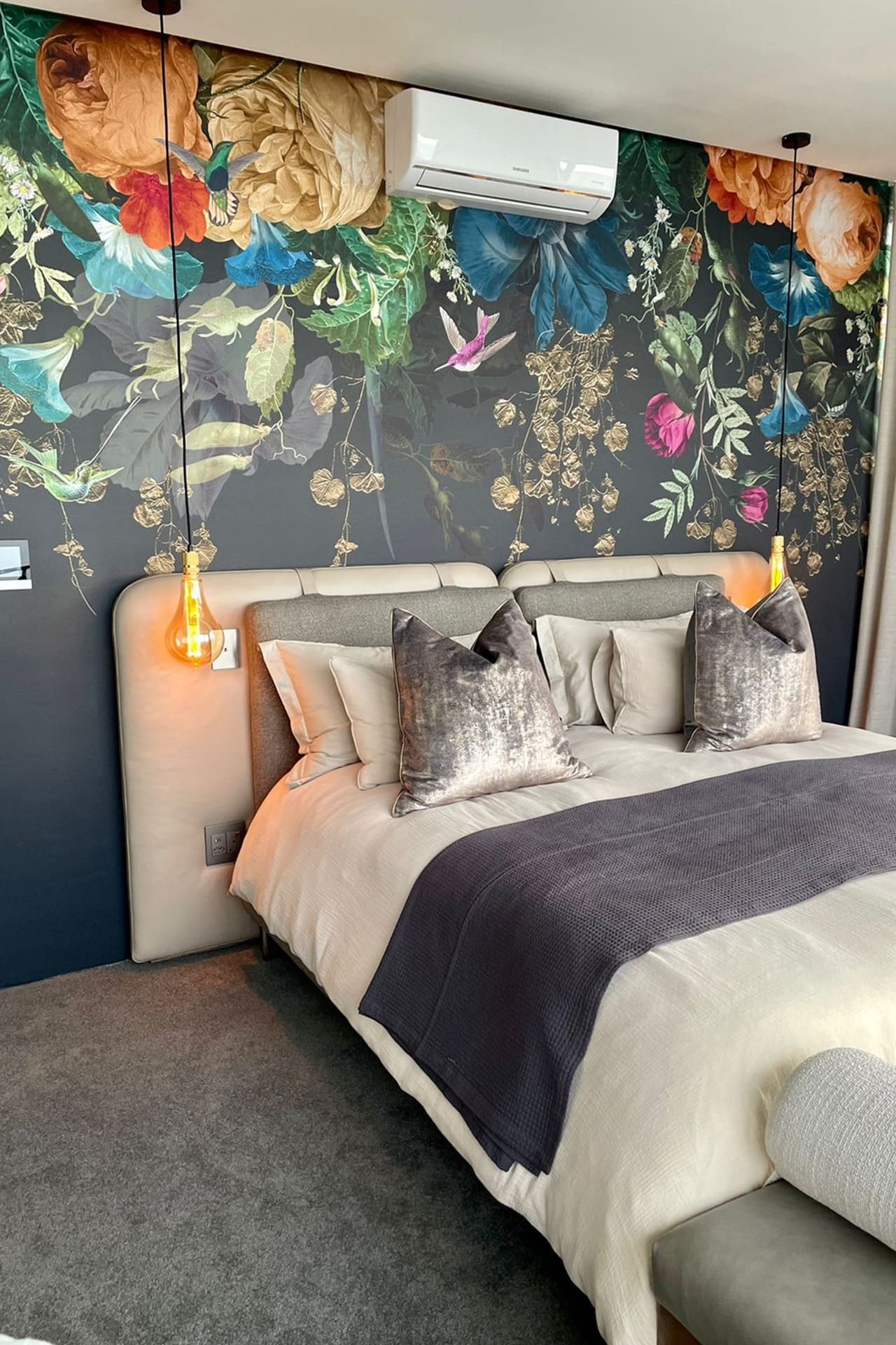 IMG-20221121-WA0028 The wallpaper features a large floral mural in vibrant colors, including rich reds, deep purples, bright yellows, lush greens, and subtle blues. The intricate design showcases a variety of flowers and leaves, creating a bold and lively backdrop for the bedroom.