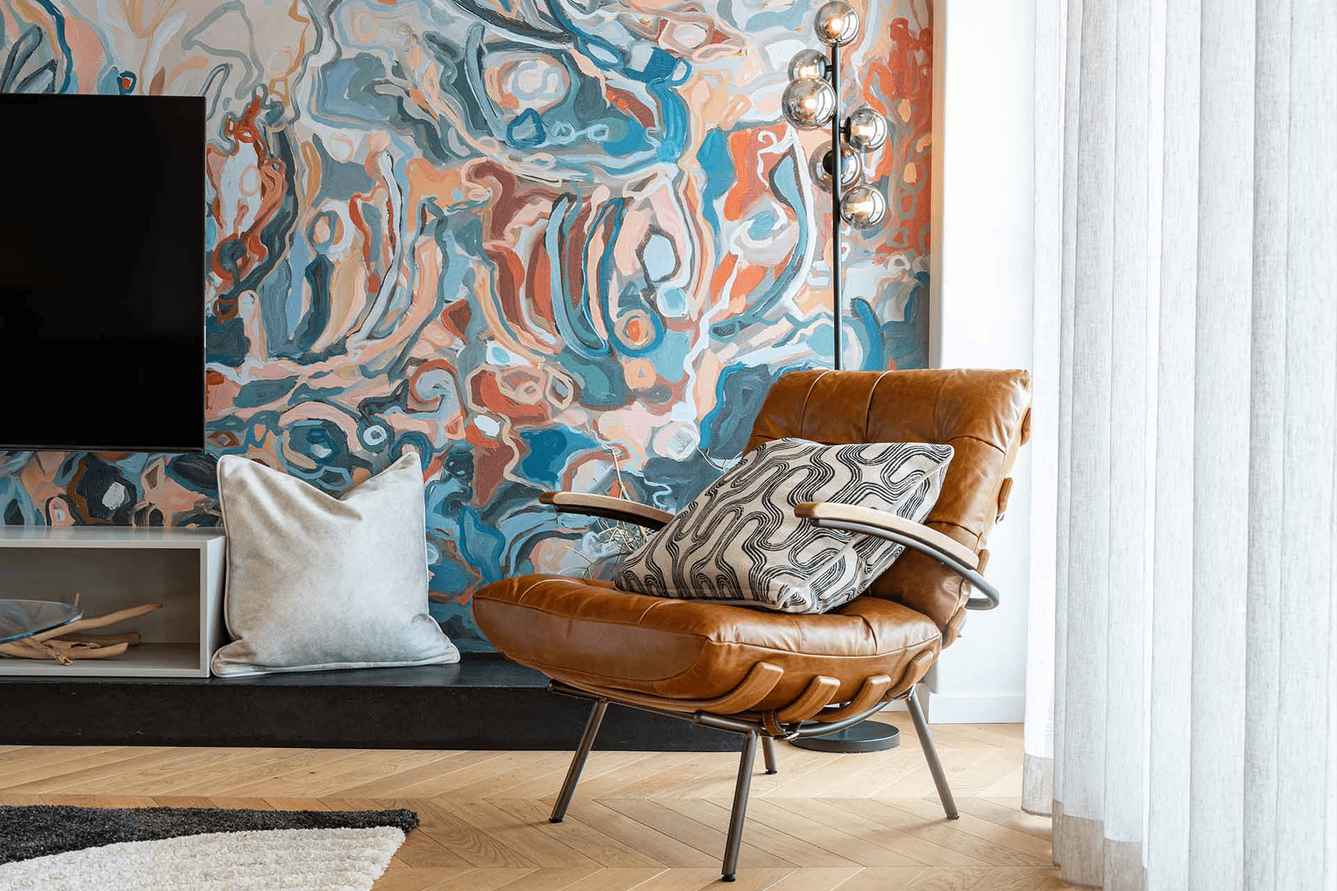 Living Room - CS&Co HVDM Pincushion Protea The wallpaper features an abstract mural with swirling colors of blue, pink, and orange. Elements include fluid, dynamic patterns that create a sense of movement and artistic flair.