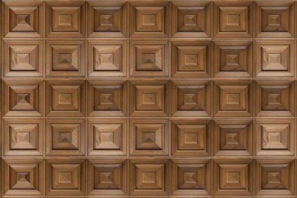 A wooden wall featuring repeating square panels, each with four concentric moulded squares arranged in a pyramid-like pattern for a 3D geometric effect. The natural brown finish highlights the visible wood grain.