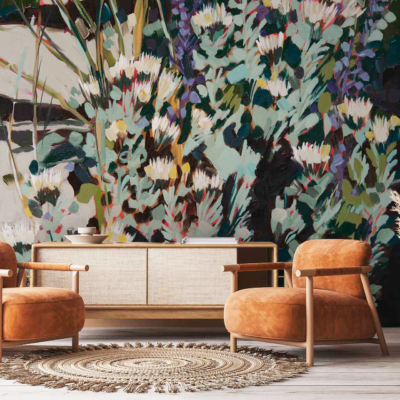 The vibrant floral mural on the back wall features Abstract Pincushion Proteas in bold colors like deep reds, bright oranges, vivid yellows, and lush greens. The design showcases intricate petals and stems with a modern artistic flair. This energetic wallpaper serves as a stunning focal point in the cozy living room.