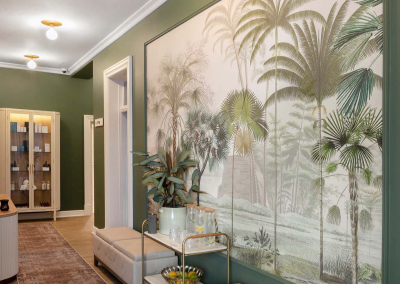 The hallway features a large tropical-themed wall mural showcasing vibrant palm trees and lush greenery. The wallpaper’s colors include various shades of green, deep blues, and touches of golden yellow, creating a vivid and inviting scene.