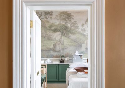 A nature-themed mural graces the far wall, featuring lush trees and rugged rocks. The wallpaper combines shades of green, earth tones, and delicate textures to create a serene forest scene, perfect for adding an inspiring touch to your creative space or personal website portfolio.