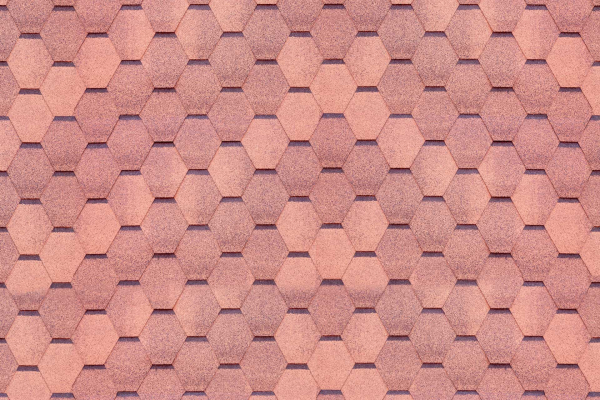 Close-up of roof with interlocking hexagonal asphalt shingles. Varying shades of reddish-brown create a textured, uniform look. Subtle shadow lines emphasize structure and color variations. Key elements: hexagonal pattern, reddish-brown shades, textured appearance, shadow lines.