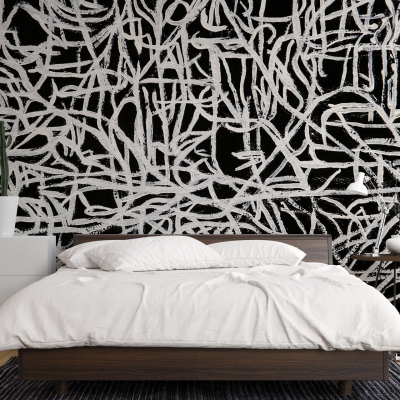 The wallpaper behind the bed is an abstract black and white mural. It features intricate patterns, bold lines, and striking contrasts between black and white elements. The design includes swirling shapes, geometric figures, and possibly some splashes or brush strokes in varying intensities of black against a white background.