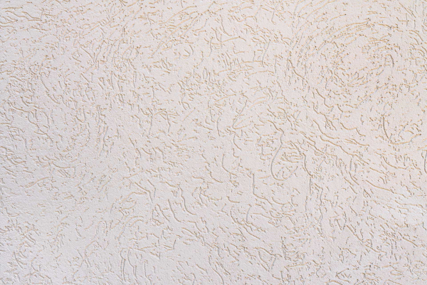 A beige textured wall with a roughed-up, stucco-like surface features random, slightly raised patterns creating an abstract design. Subtle variations in shading add depth to the texture. Keywords: beige, textured wall, roughed-up surface, stucco-like, raised patterns, abstract design, shading variations.