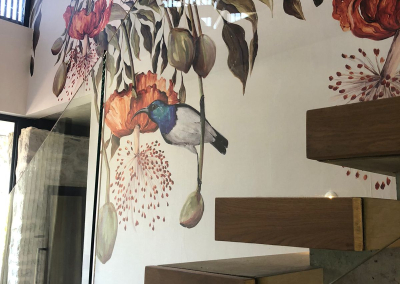 Decorative mural on the wallpaper features intricate flowers, leaves, and a colorful bird. Vibrant hues of red, blue, green, and yellow add a dynamic touch.