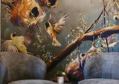 The wallpaper features a vibrant mural depicting birds and their nests amidst lush green foliage. The natural setting highlights elements such as branches, leaves, and various bird species. Colors include rich greens, browns, and hints of vibrant hues from the birds' feathers.